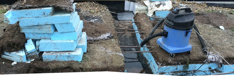 A green roof stripped back to the waterproofing membrane for electronic leak detection: stacked insulation boards, removed substrate and standing water on the exposed membrane